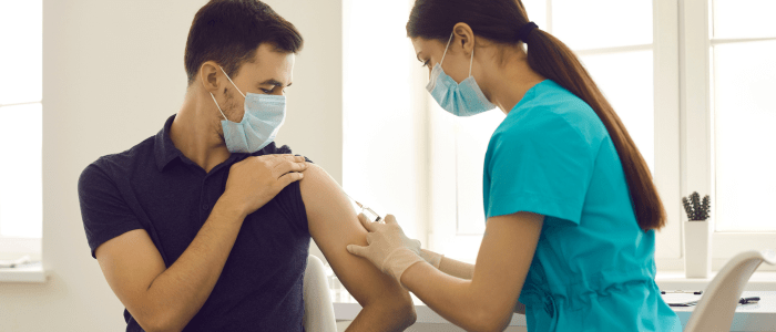 A woman in blue scrubs injects a vaccine into the upper arm of a man wearing a navy t-shirt. To represent that a RWD study shows fewer heart issues after COVID-19 vaccine.